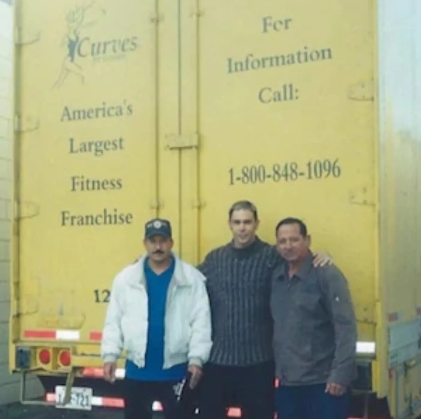 Shane James with two colleagues in front of a Curves for Women transport trailer