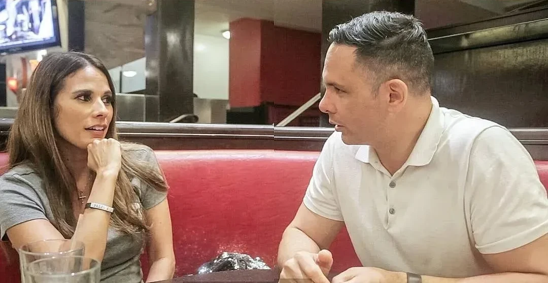 Shane James in conversation with a woman across a red diner booth