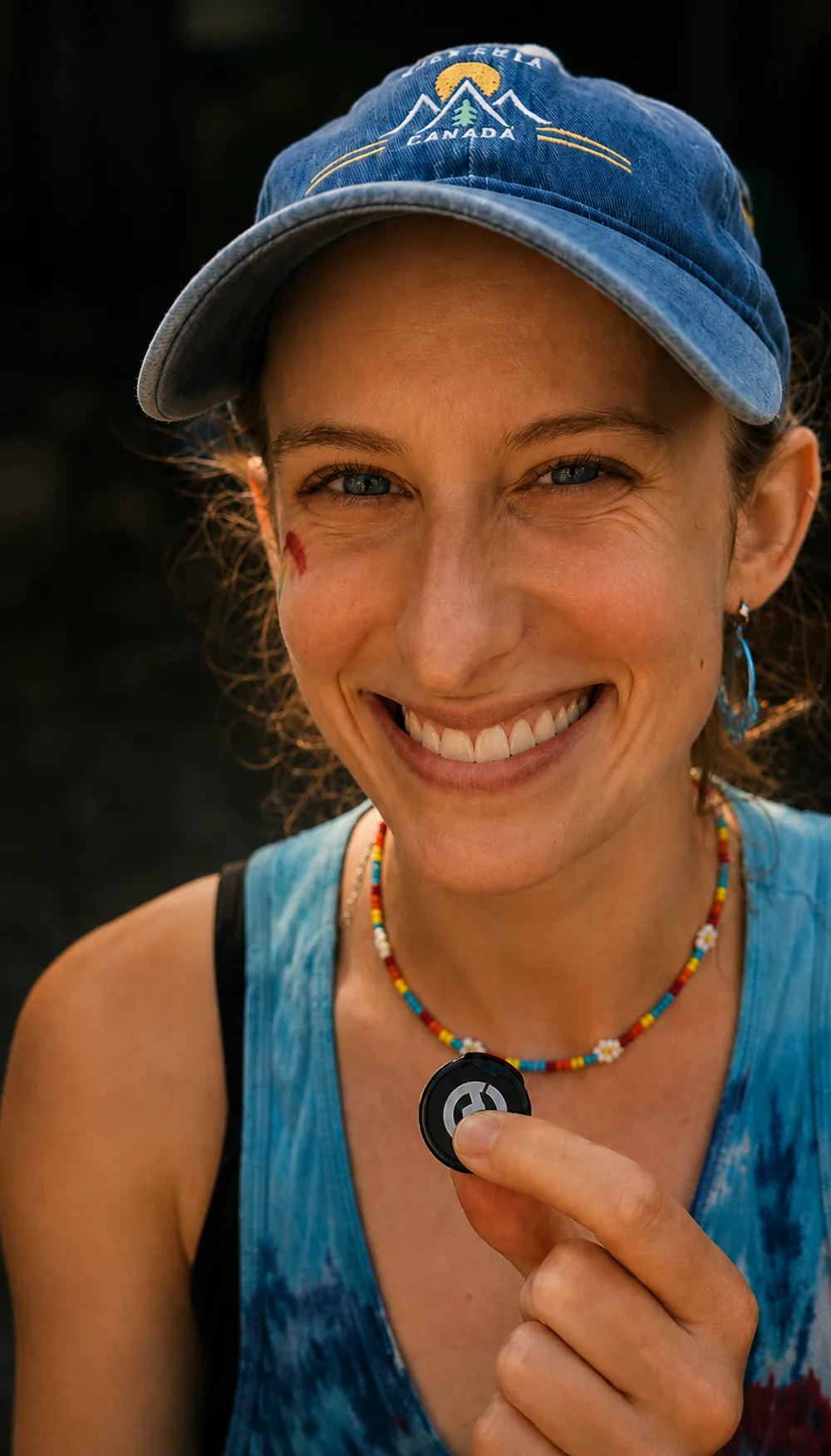 A woman in a blue cap smiling as she holds up a small Be Human token